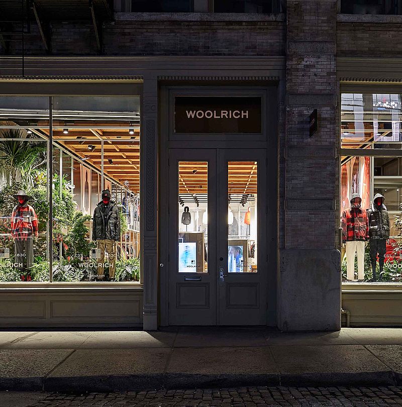 Illuminated Woolrich flagship store facade at night with mannequins in window display
