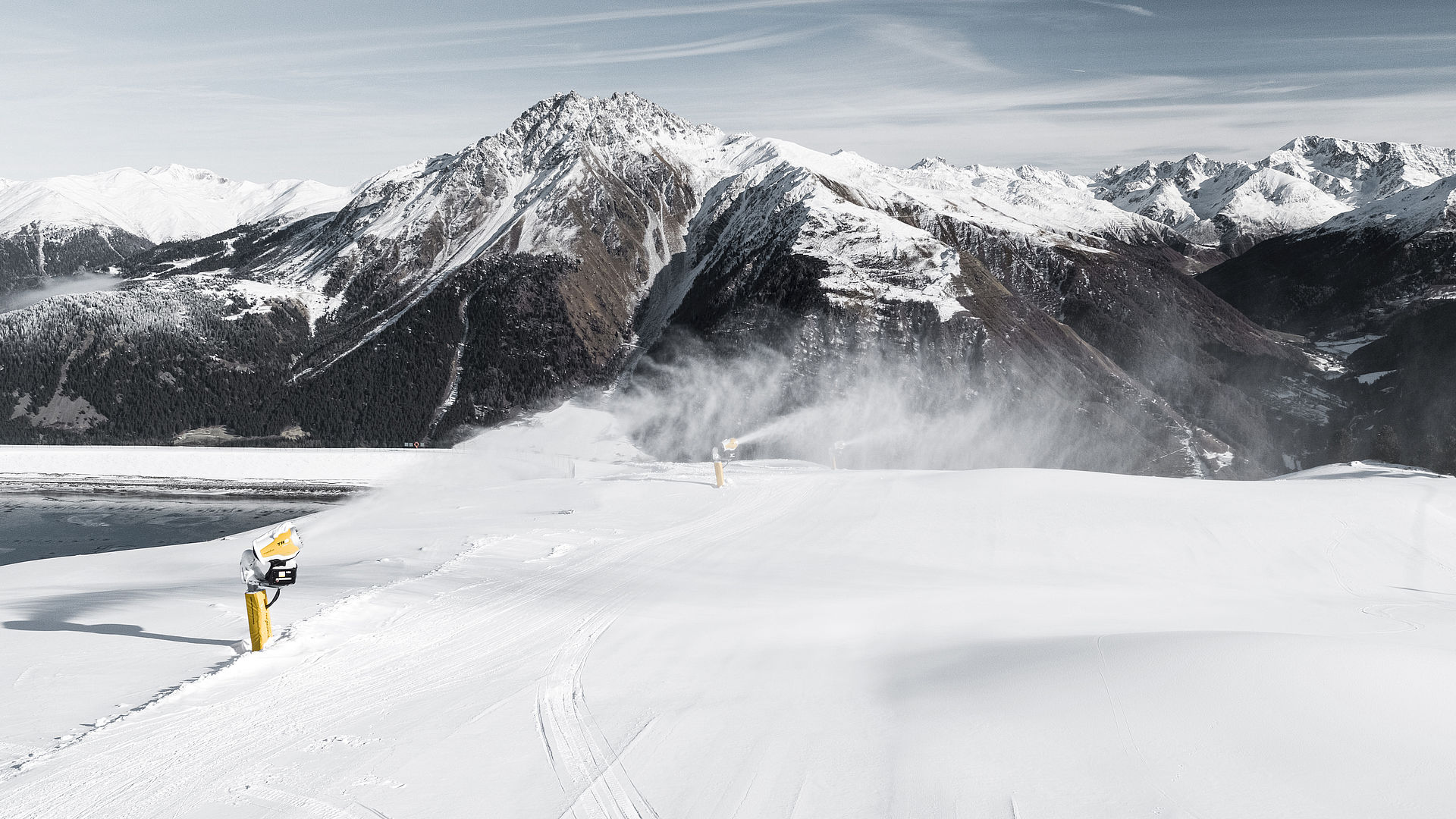 Canon à neige TechnoAlpin enneigant une piste de ski avec panorama alpin en arrière-plan
