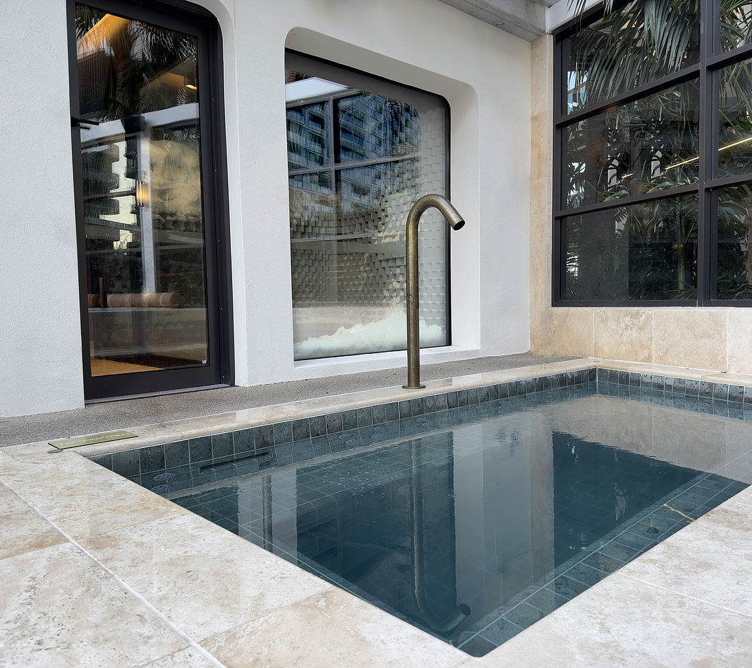 Small plunge pool with blue tiles and brass faucet next to window with snowroom view