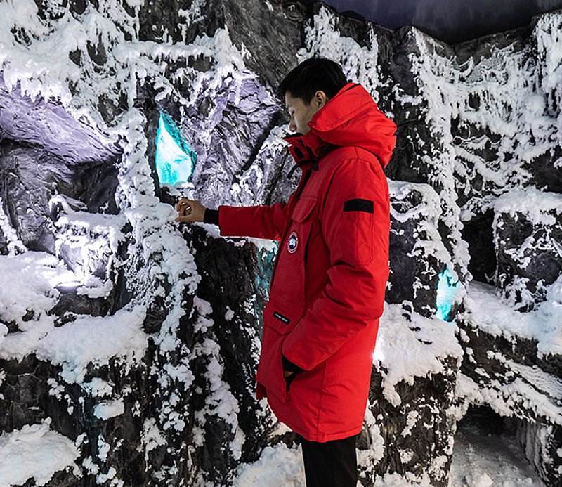 Mann in roter Canada Goose Parka in Indoor-Eishöhle mit beleuchteten blauen Eiskristallen.