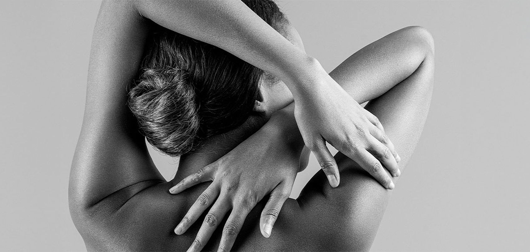 Black and white photo of woman's back with crossed arms, aesthetic wellness motif
