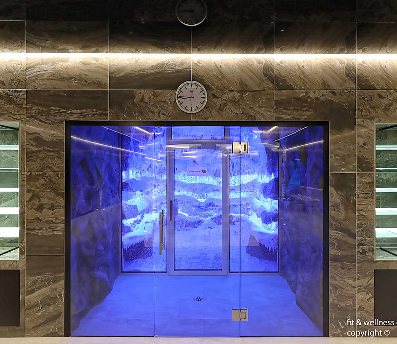 Elegant glass door entrance to blue-lit snow cabin with marble wall and illuminated display cases.