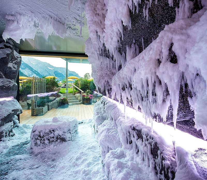 Innenansicht einer Schneegrotte mit Eiszapfen und Panoramafenster mit Blick auf Berglandschaft.