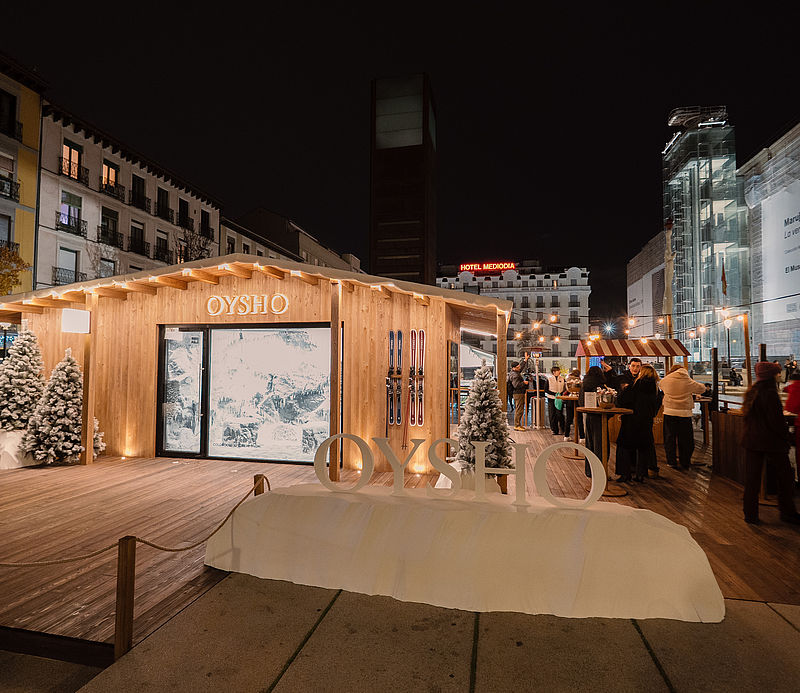 Oysho Pop-up Holzchalet bei Nacht mit Besuchern und Schneekulisse auf urbanem Platz in Madrid