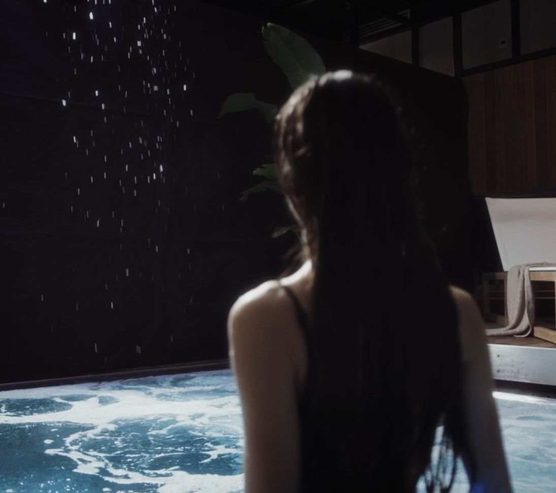 Woman from behind in front of illuminated pool with falling snow and starry sky effect