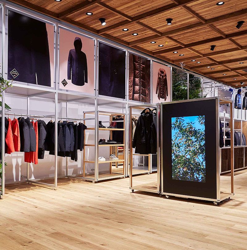 Modern Woolrich store with plant wall, wooden floor, jacket presentation and digital display