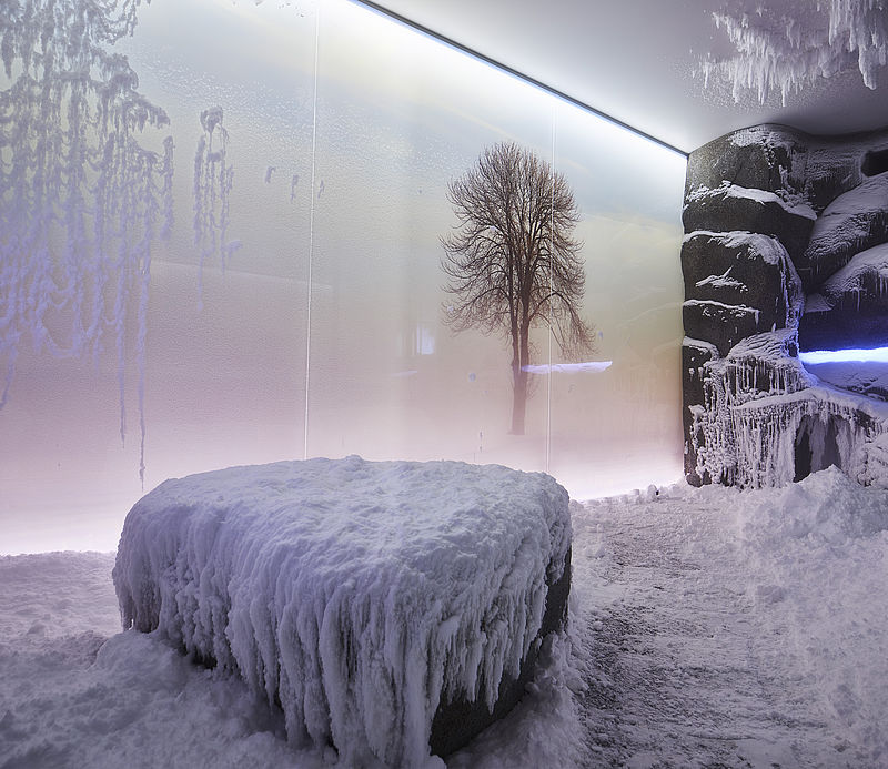 Snow chamber with icy bench, winter tree motif on wall and icicles.
