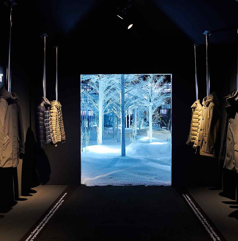 Woolrich-Ausstellungsgang mit Parkas und Blick auf beleuchteten Schneewald-Raum