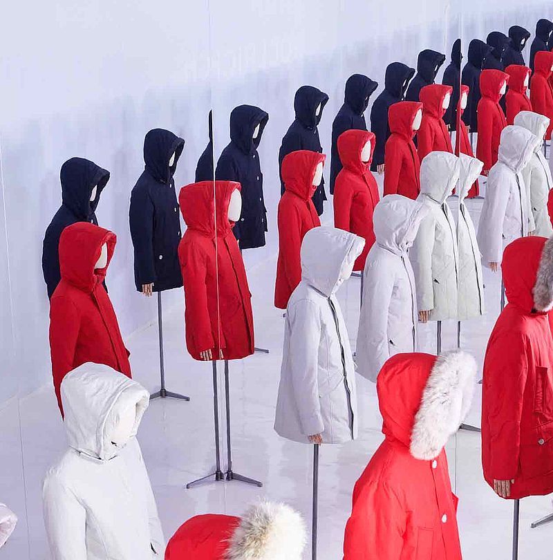 Lange Reihen roter, weißer und schwarzer Parkas auf Schaufensterpuppen in weißem Raum