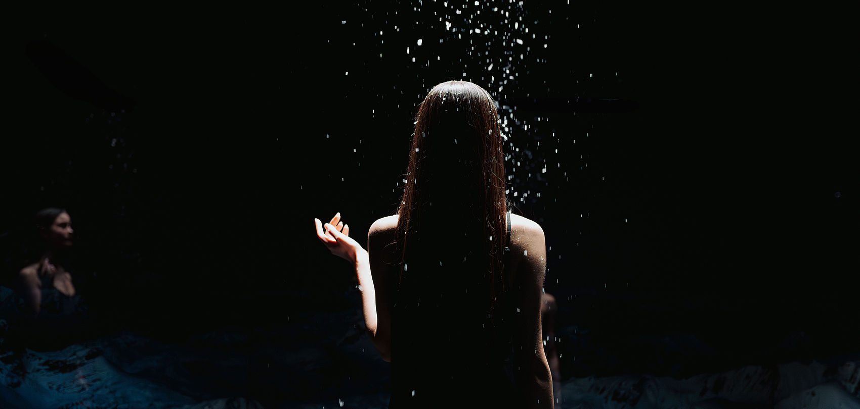 Silhouette of a woman from behind under softly falling snow in the dark SnowRoom
