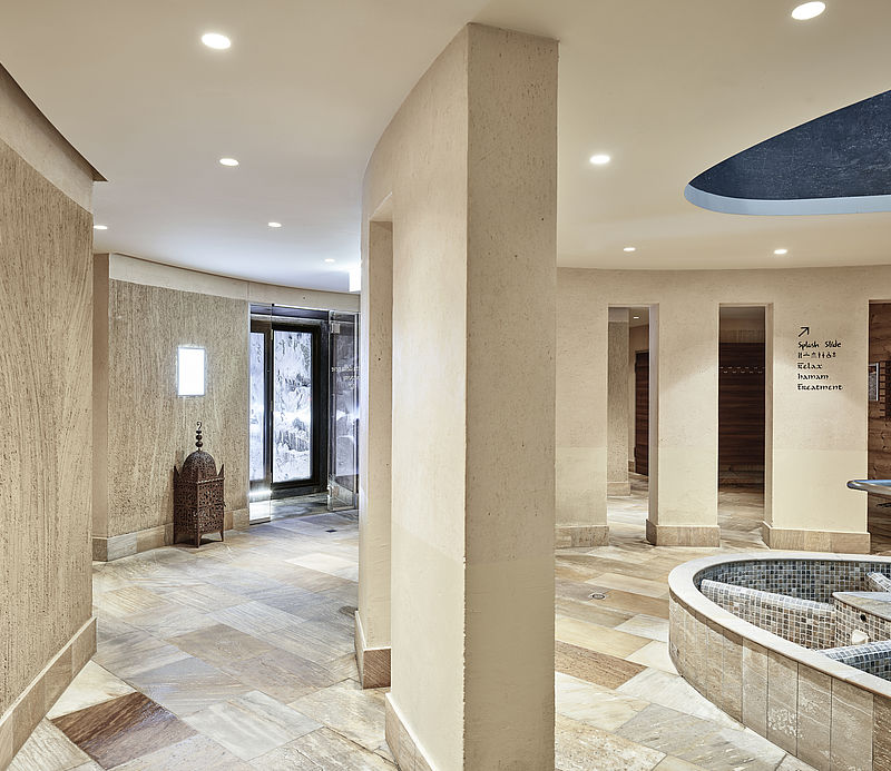 Eleganter Spa-Bereich mit Travertin-Säulen, Steinboden und rundem Becken vor Eingang zum Schneeraum.