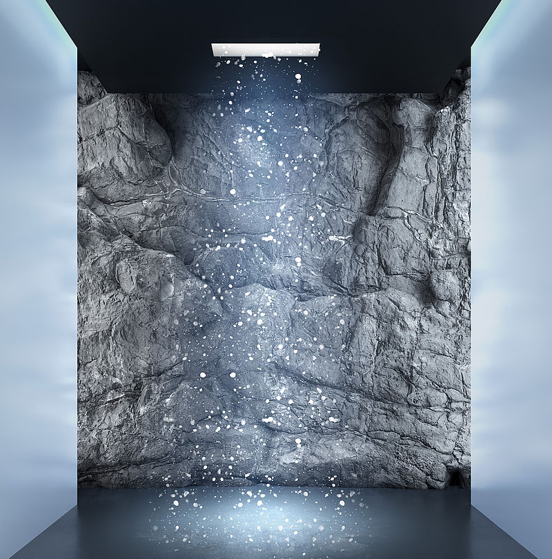 TechnoAlpin SnowSky erzeugt atmosphärischen Kunstschneefall in dunklem Spa-Raum mit Felswand