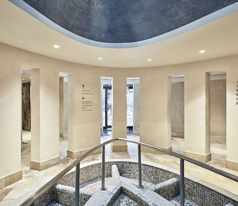Runder Spa-Vorraum mit Säulen, Wegweisern zu Sauna und Hamam sowie zentralem Mosaikbecken.
