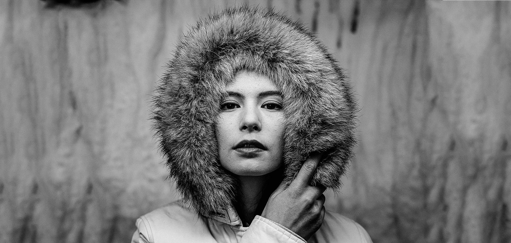 Black and white portrait of woman with fur hood, serious gaze into camera