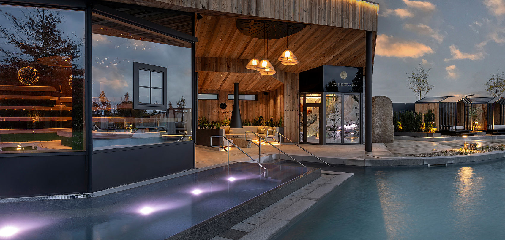 Illuminated wooden pavilion with pool and steps into water at dusk