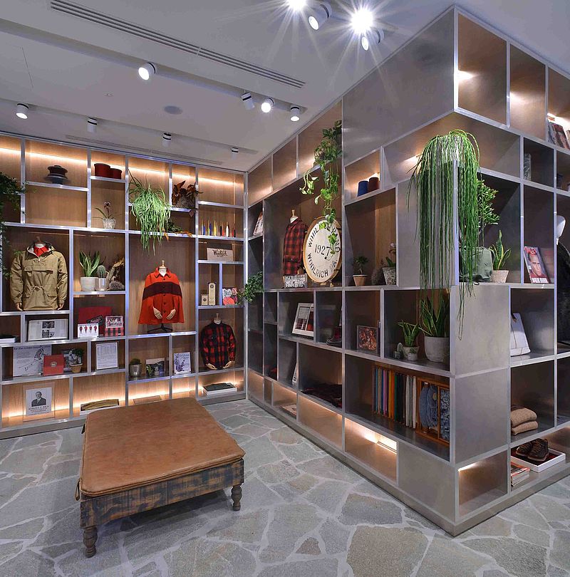 Woolrich store with wall shelf of vintage jackets, plants and brand memorabilia on natural stone floor