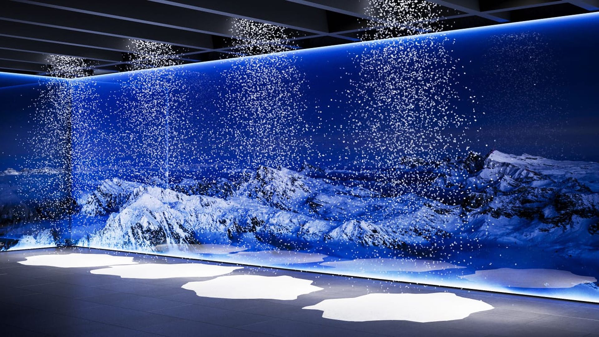 Indoor snow room with blue illuminated mountain panorama wall and falling artificial snow