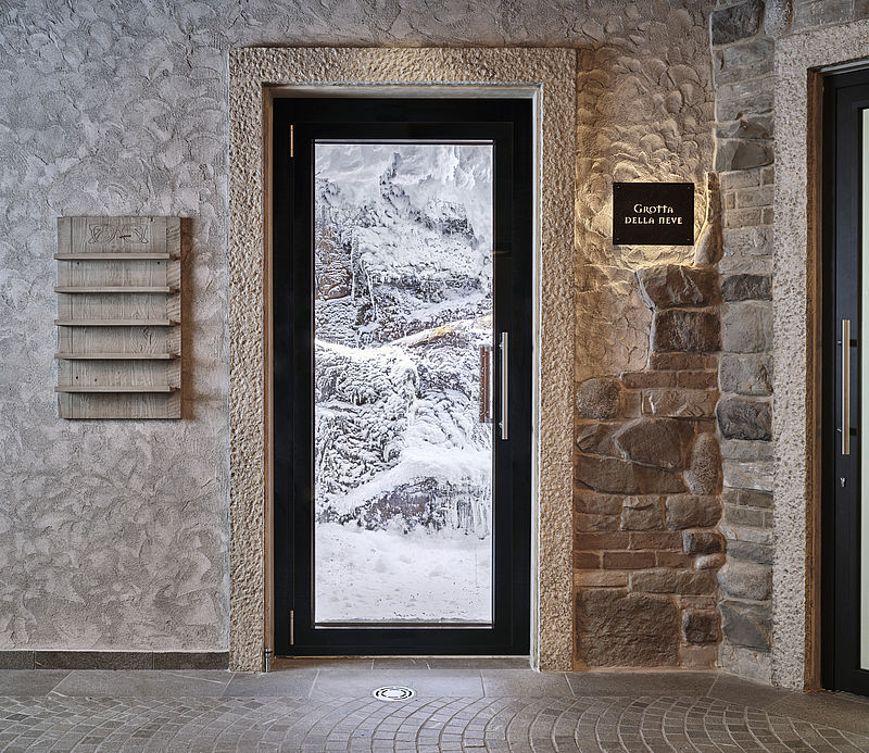 Eingangstür zur Grotta della Neve mit Blick auf vereiste Schneelandschaft in rustikalem Spa-Ambiente.