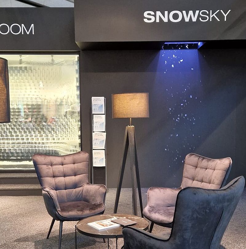 TechnoAlpin SnowSky Messestand mit Lounge-Sesseln und aktivem Deckenbeschneier beim Kunstschneefall