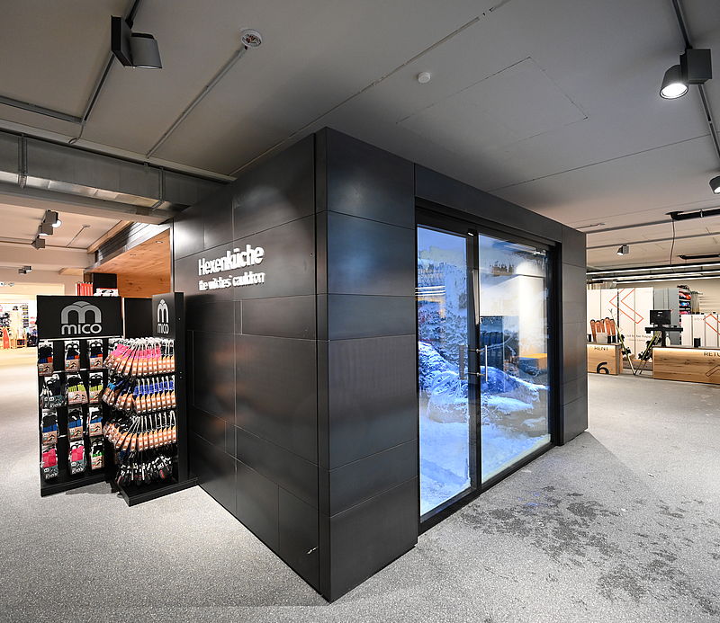 Entrance to Hexenküche snow chamber in a ski rental shop with product display.