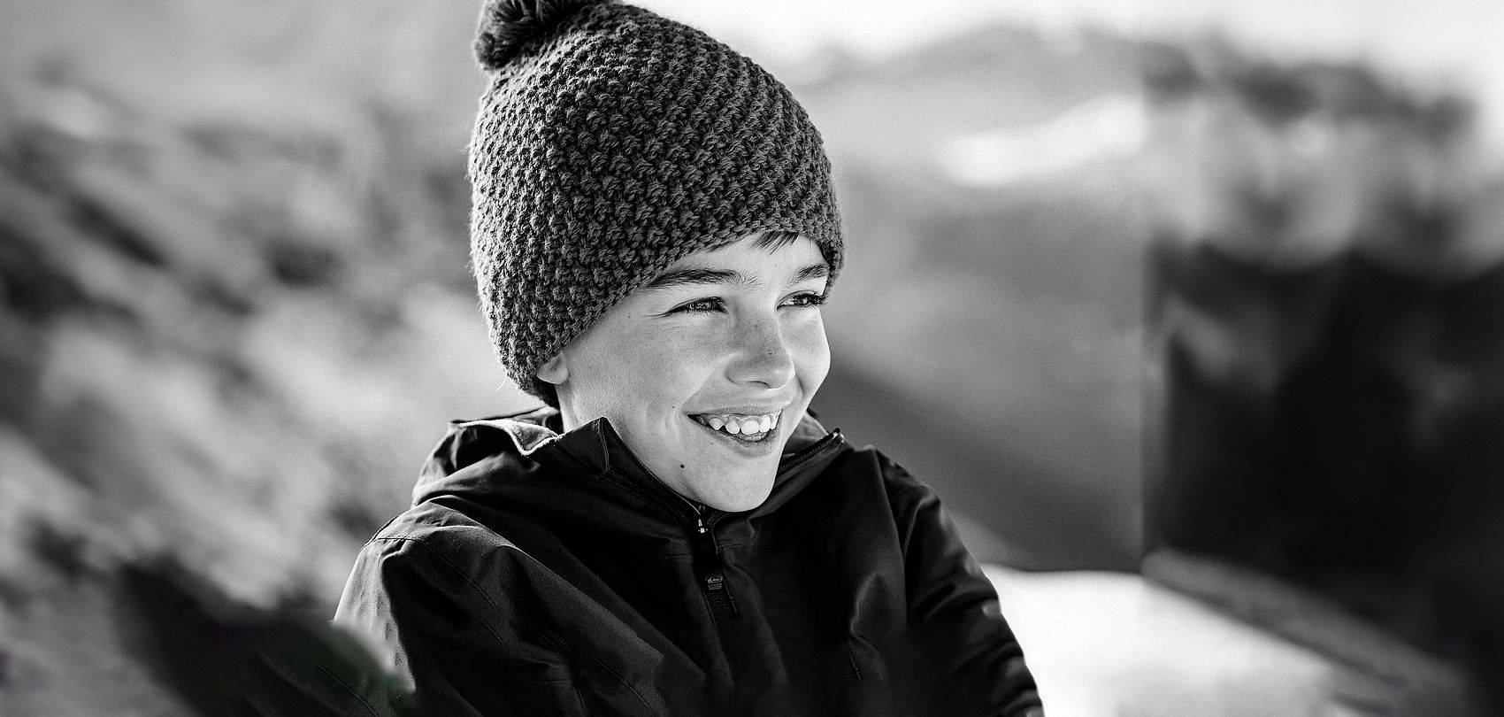 Black and white photo of laughing boy with knitted hat in mountain scenery