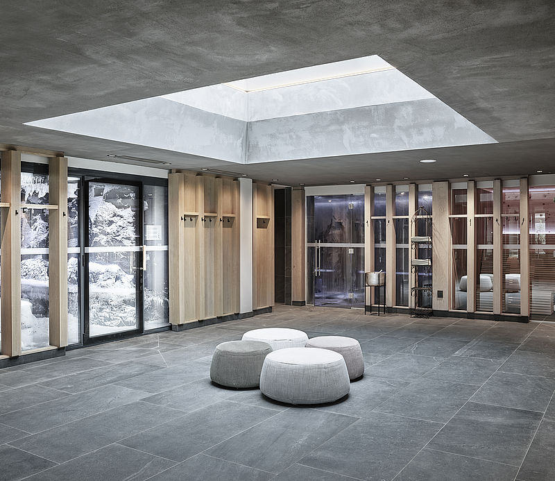 Modern spa relaxation area with ottomans, view of snow room, sauna and wooden elements.
