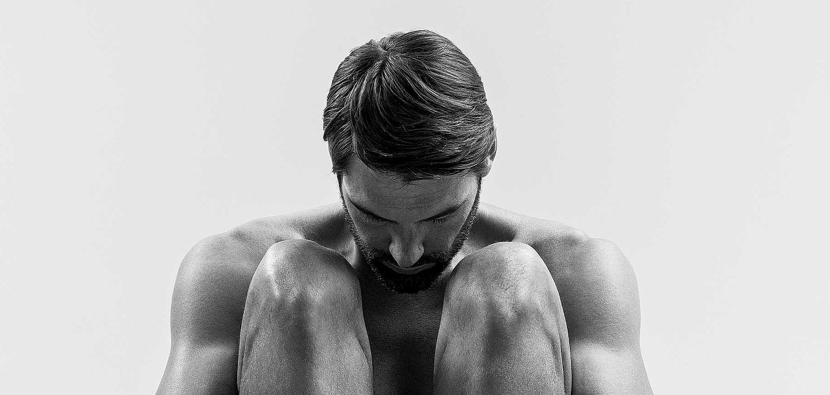 Black and white photo of seated muscular man with bowed head