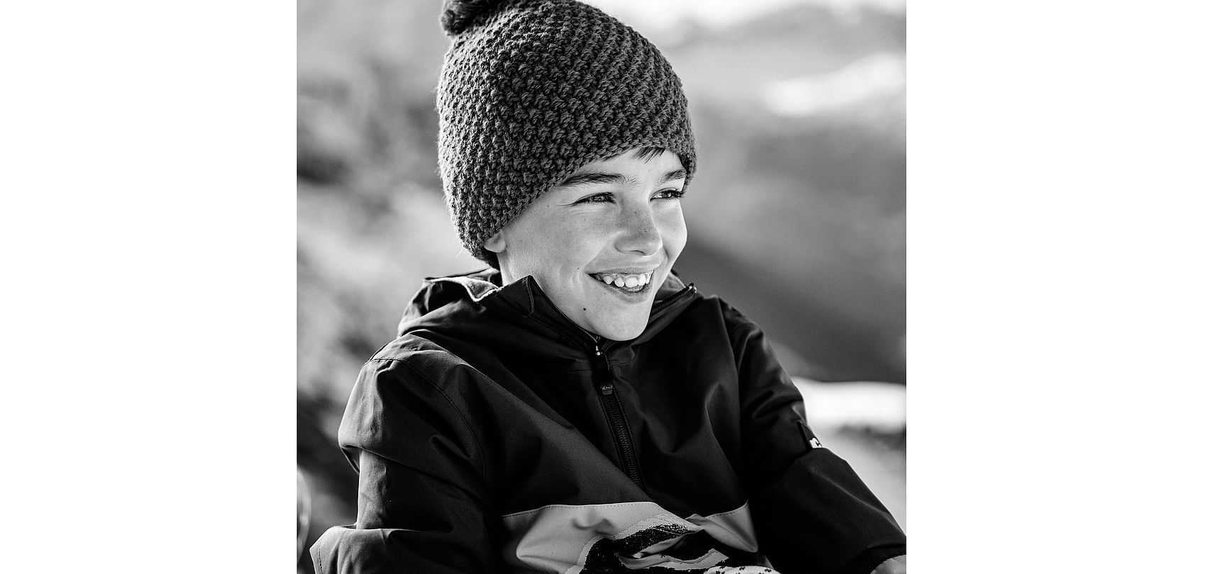 Black and white portrait of laughing boy with bobble hat in the mountains