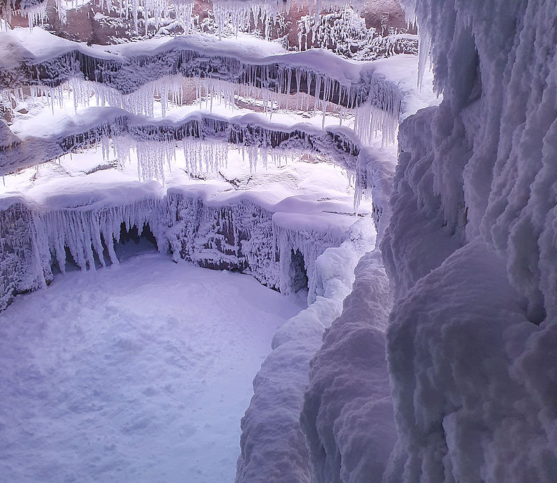 Vista di dettaglio di una grotta nevada con formazioni di ghiaccio a terrazze e lunghe stalattiti.