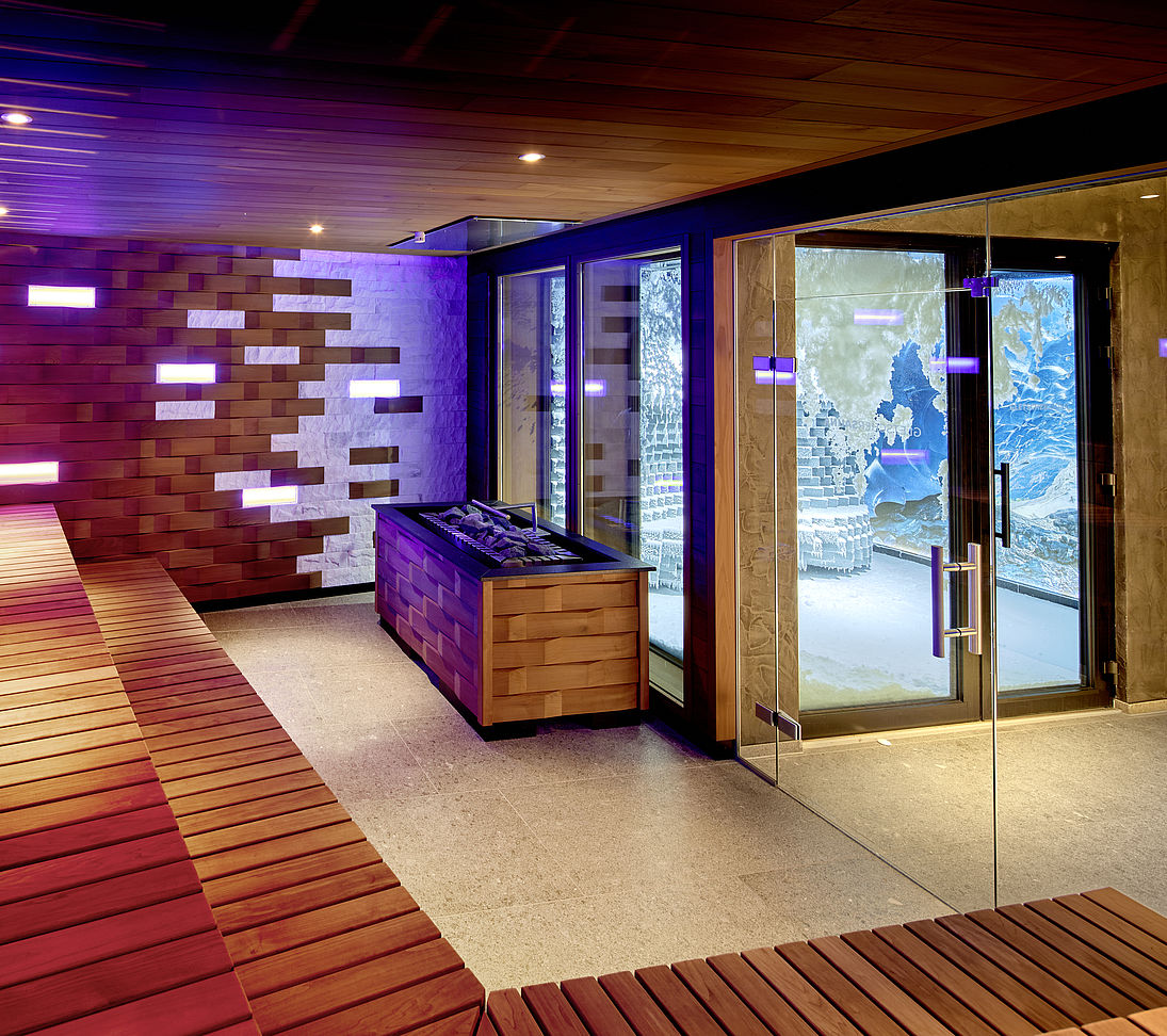 Modern sauna with wooden benches, lilac light accents and glass door with view of snow room