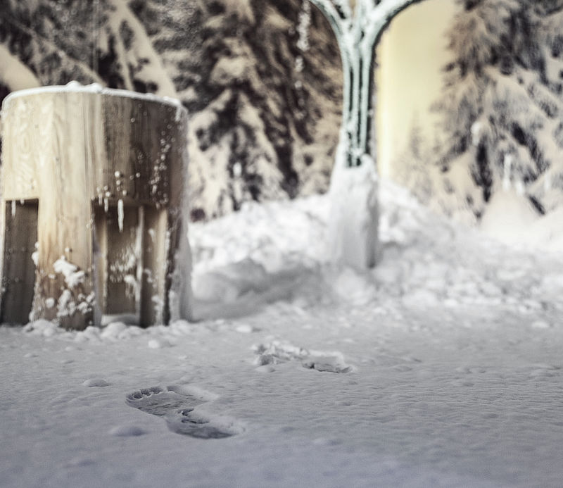 Holzhocker im Schneeraum mit Fußspuren im frischen Pulverschnee und winterlicher Wandgestaltung.